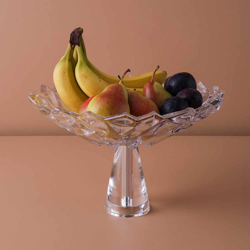 Clear glass fruit bowl with bananas, pears, and plums on a brown background